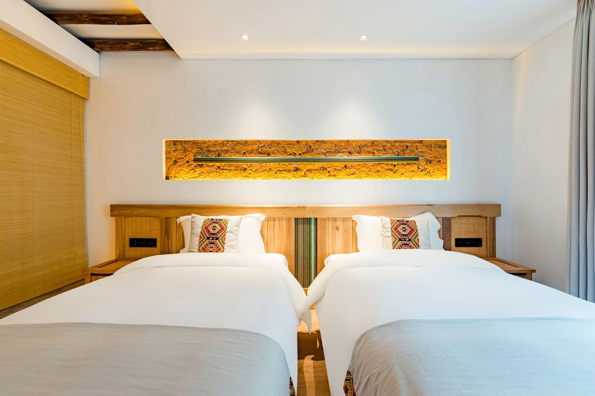 A modern hotel room with two beds, a wooden headboard, a large abstract artwork above the beds, and a view of the city through the window.