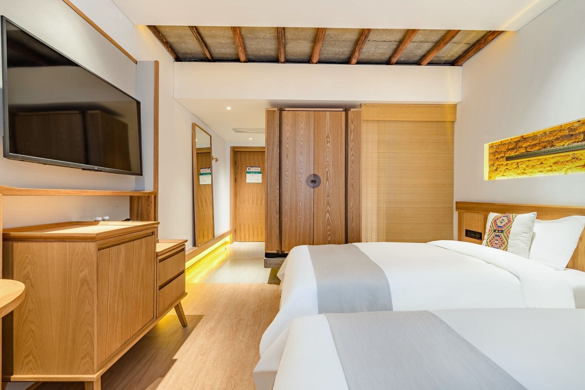 Habitación de hotel con una cama grande, televisión montada en la pared, muebles de madera y techo con vigas a la vista.
