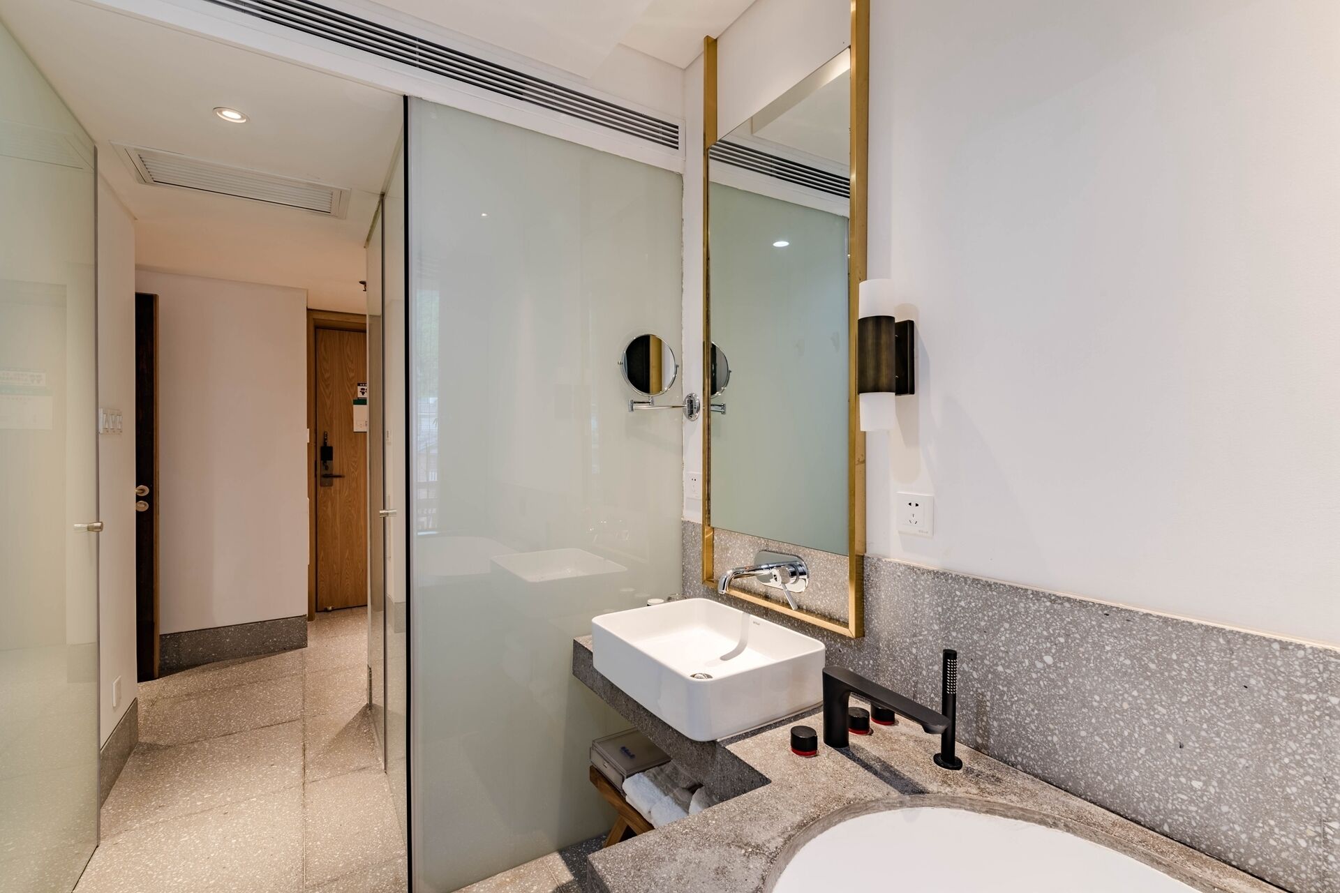 A modern bathroom with a glass partition, a white sink, a large mirror, and a shower area.