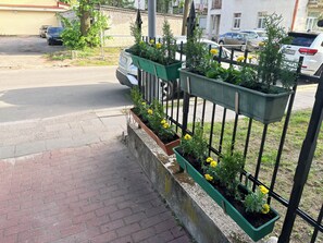 A street view with a row of planters along a sidewalk, a parked car, and a building in the background.