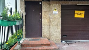 Un bâtiment avec une porte marron, une porte de garage sur laquelle est apposée une enseigne, et un petit escalier en briques menant à l’entrée.