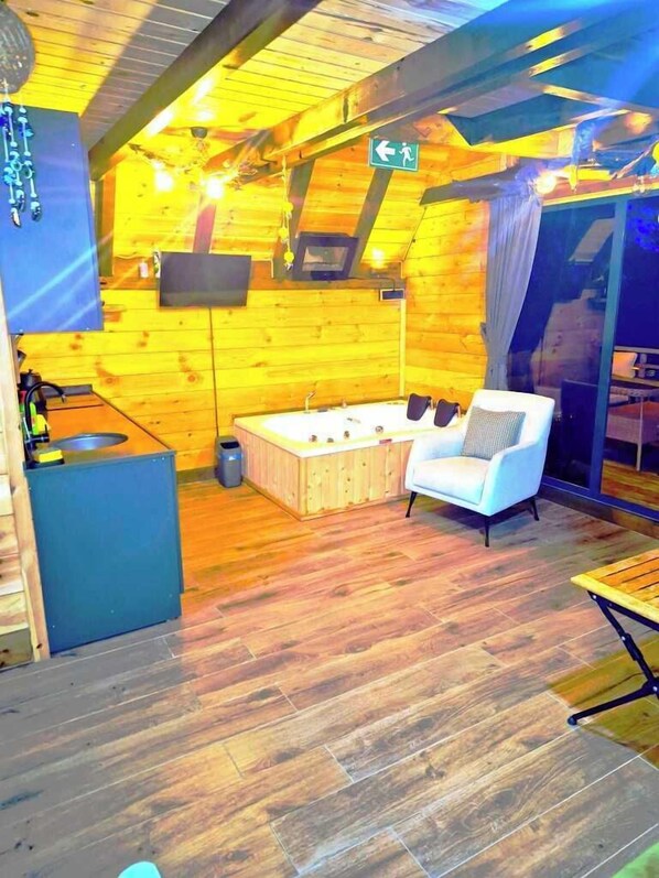 Interior acogedor de una cabaña de troncos con piso de madera, un sofá blanco, un banco de madera, una mesita y un ventanal grande.