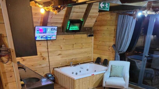 Una habitación acogedora con detalles de madera, una bañera grande, un pequeño sofá, una mesa y un televisor montado en la pared.