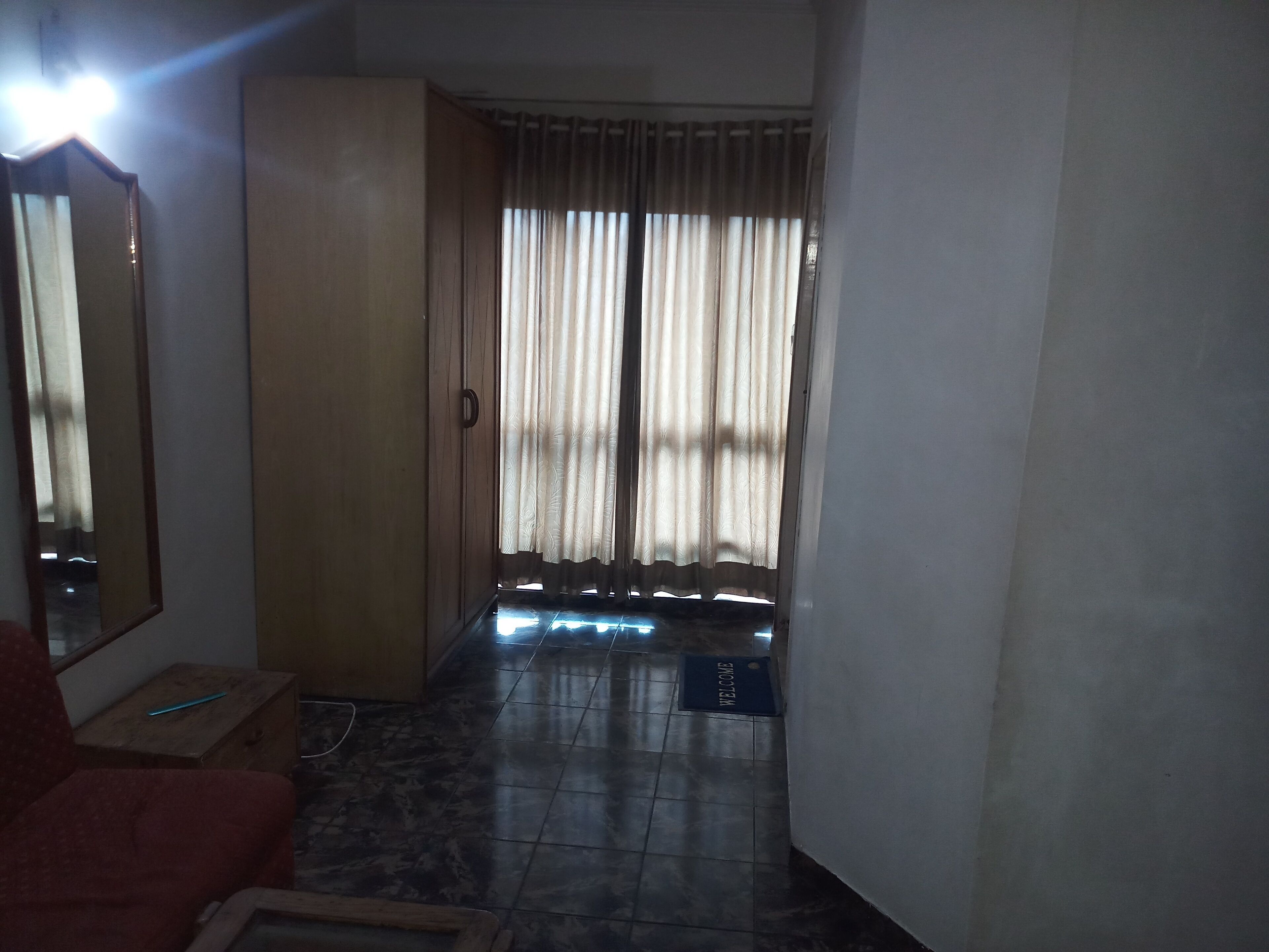 Una habitación con armario, una silla roja, suelo de baldosas y una ventana con cortinas.