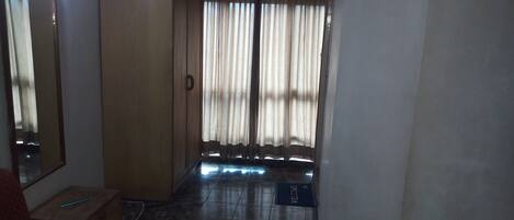 Una habitación con armario, una silla roja, suelo de baldosas y una ventana con cortinas.