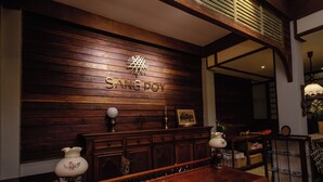 A wooden wall with the name 'SANGPOY COTTAGE' and a decorative emblem. There is a wooden bench with a lamp on each end.