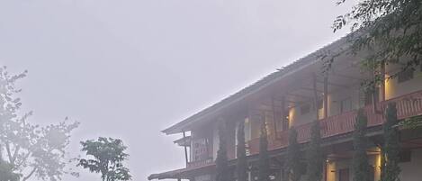 Un edificio con varios balcones, un sendero pavimentado y una zona ajardinada con bancos.