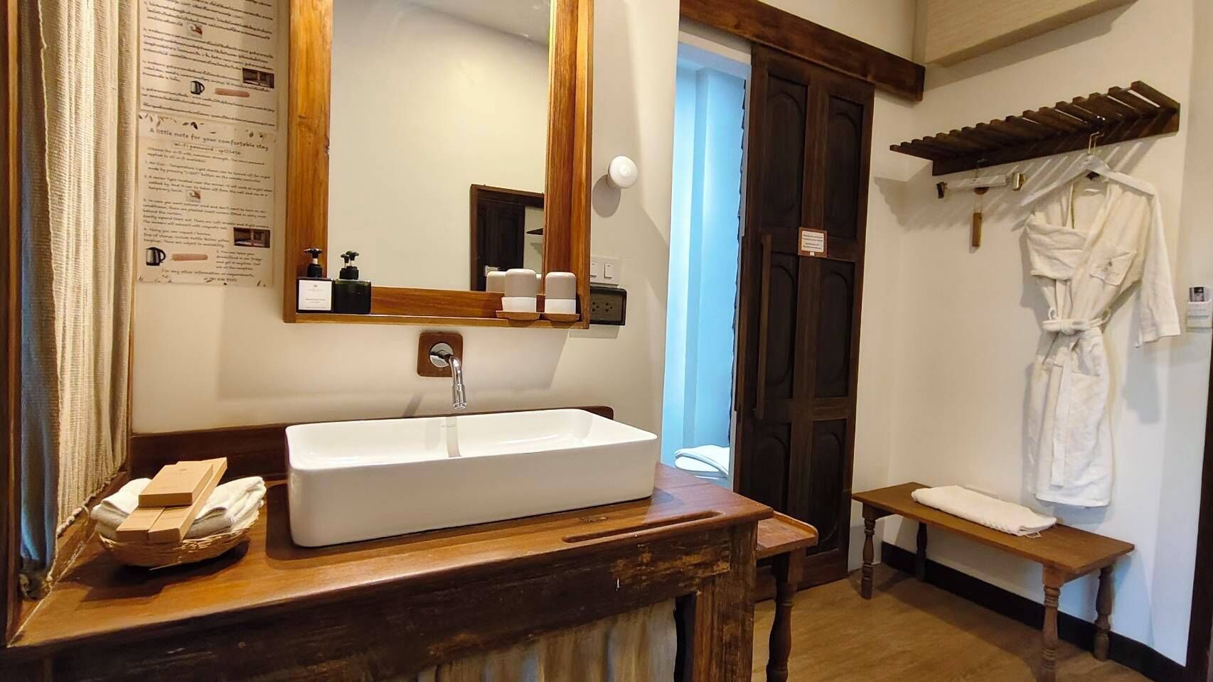A bathroom with a wooden vanity, a large mirror, a sink, and a bench.