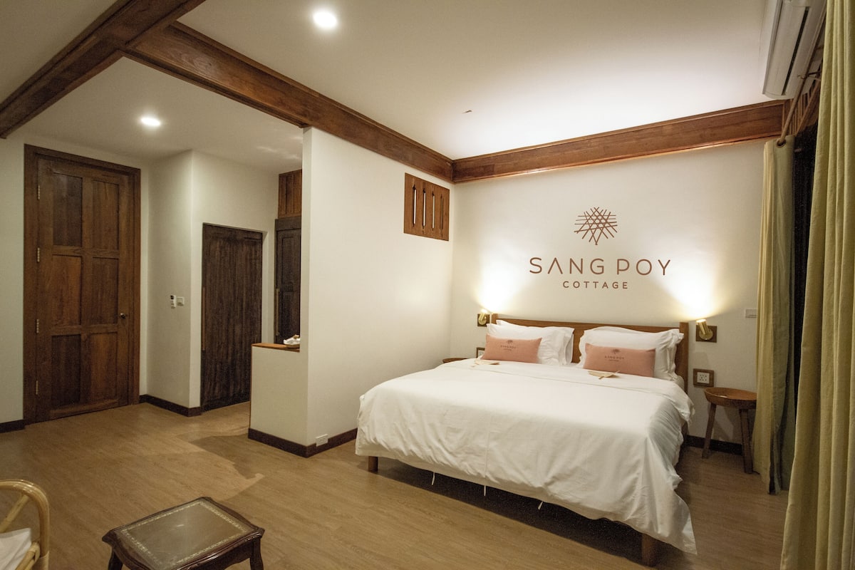 Ein Schlafzimmer mit einem großen Bett, Holzbalken, einem an der Wand befestigten Schild und einem kleinen Tisch.