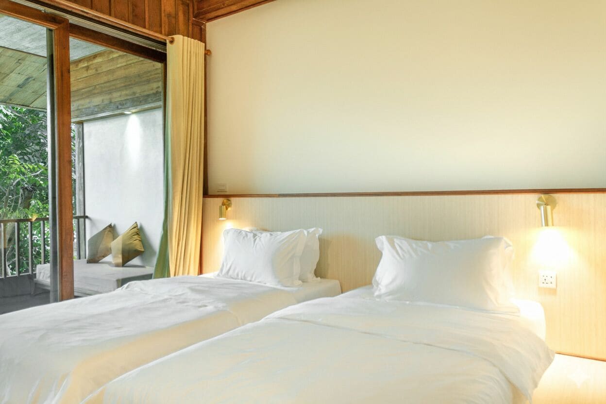 Habitación de hotel con dos camas, un balcón y vistas a zonas verdes.