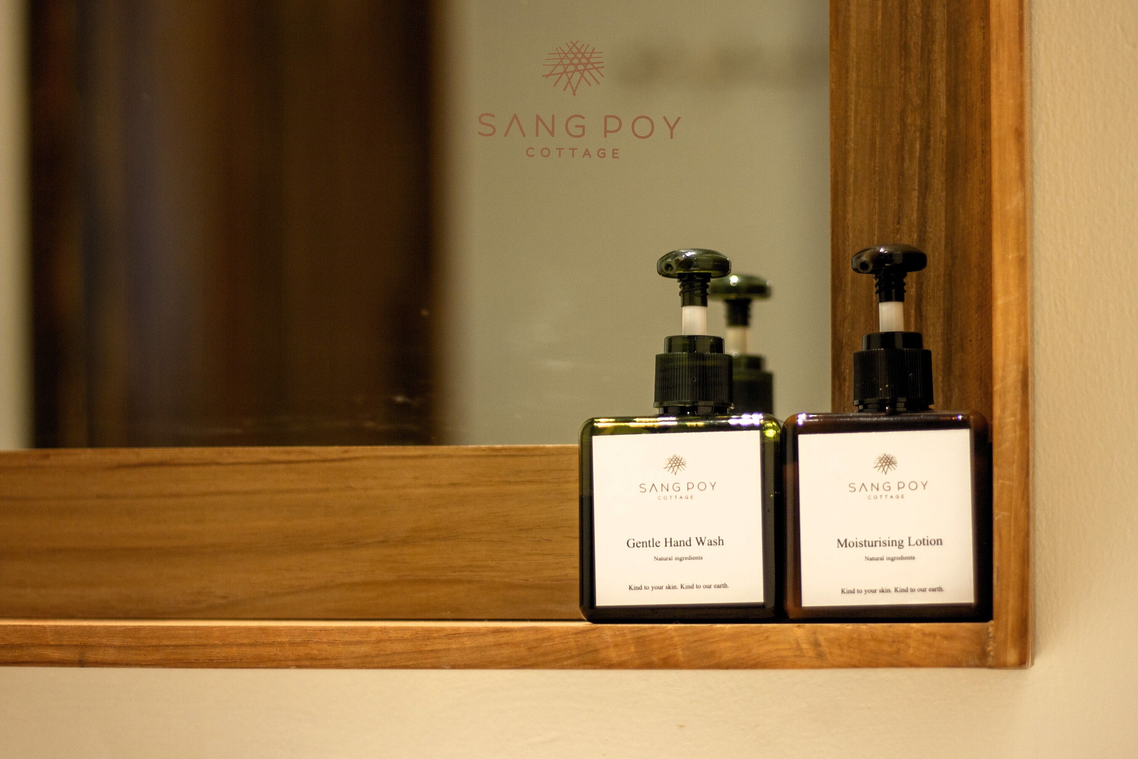 Two bottles of SangPoy Cottage products, a hand wash and a moisturizing lotion, on a wooden shelf.