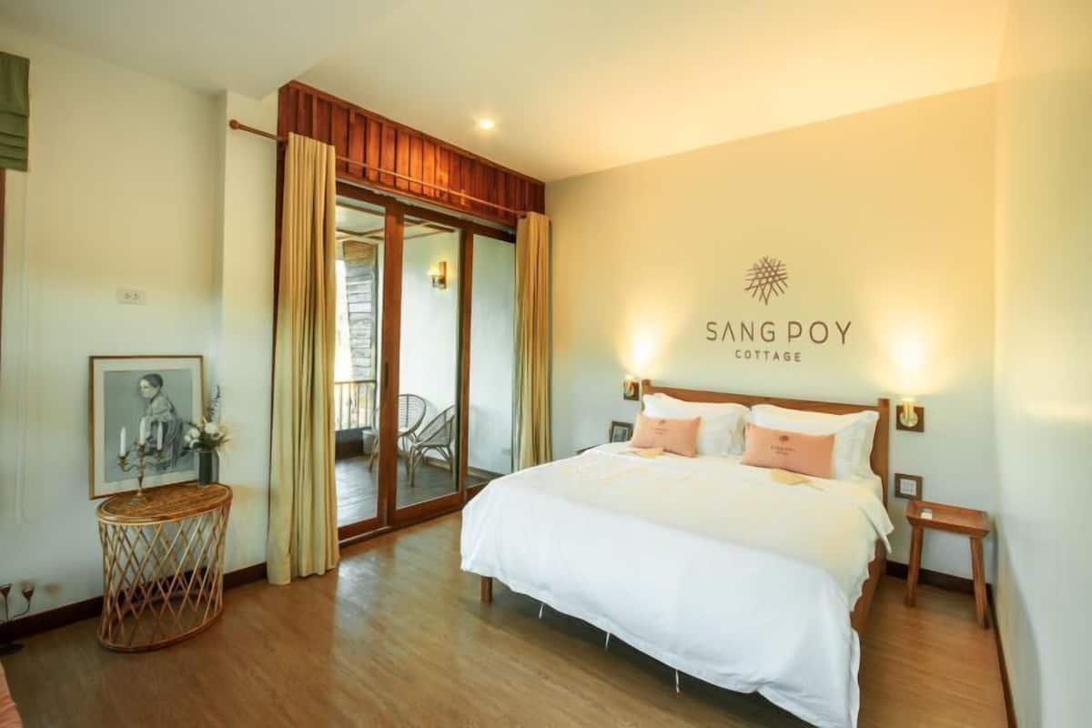 Ein Schlafzimmer mit einem großen Bett, Holzboden, einer Glastür zum Balkon und einem an der Wand befestigten Schild mit der Aufschrift 'SANG POY COTTAGE'.