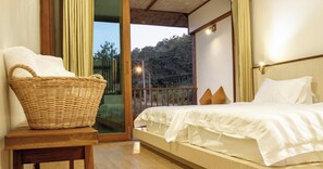Ein Schlafzimmer mit einem Bett, einem Korbwäscheschrank und Blick auf Bäume durch eine Glastür.