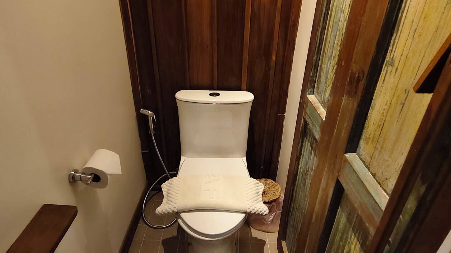 A toilet with a white seat and lid, a toilet paper holder, and a shower hose.