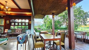 A wooden deck with tables and chairs, a fan, and a view of greenery.