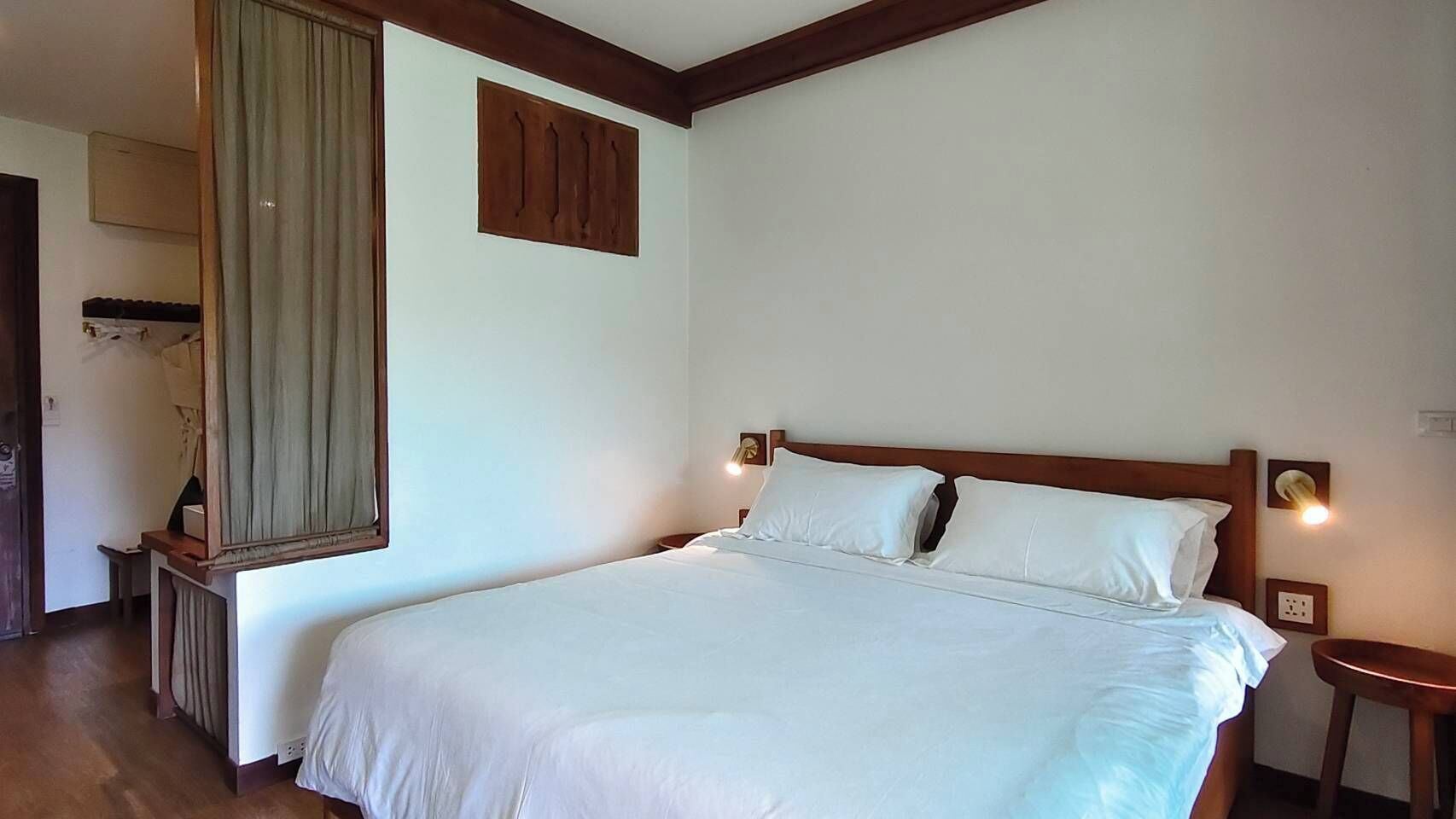 A neatly made bed in a room with a wooden headboard, a bedside table, and a wall-mounted light fixture.