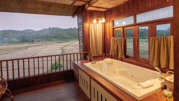 Eine Holzhütte mit einer großen Badewanne und einem Balkon mit Blick auf ein Feld.