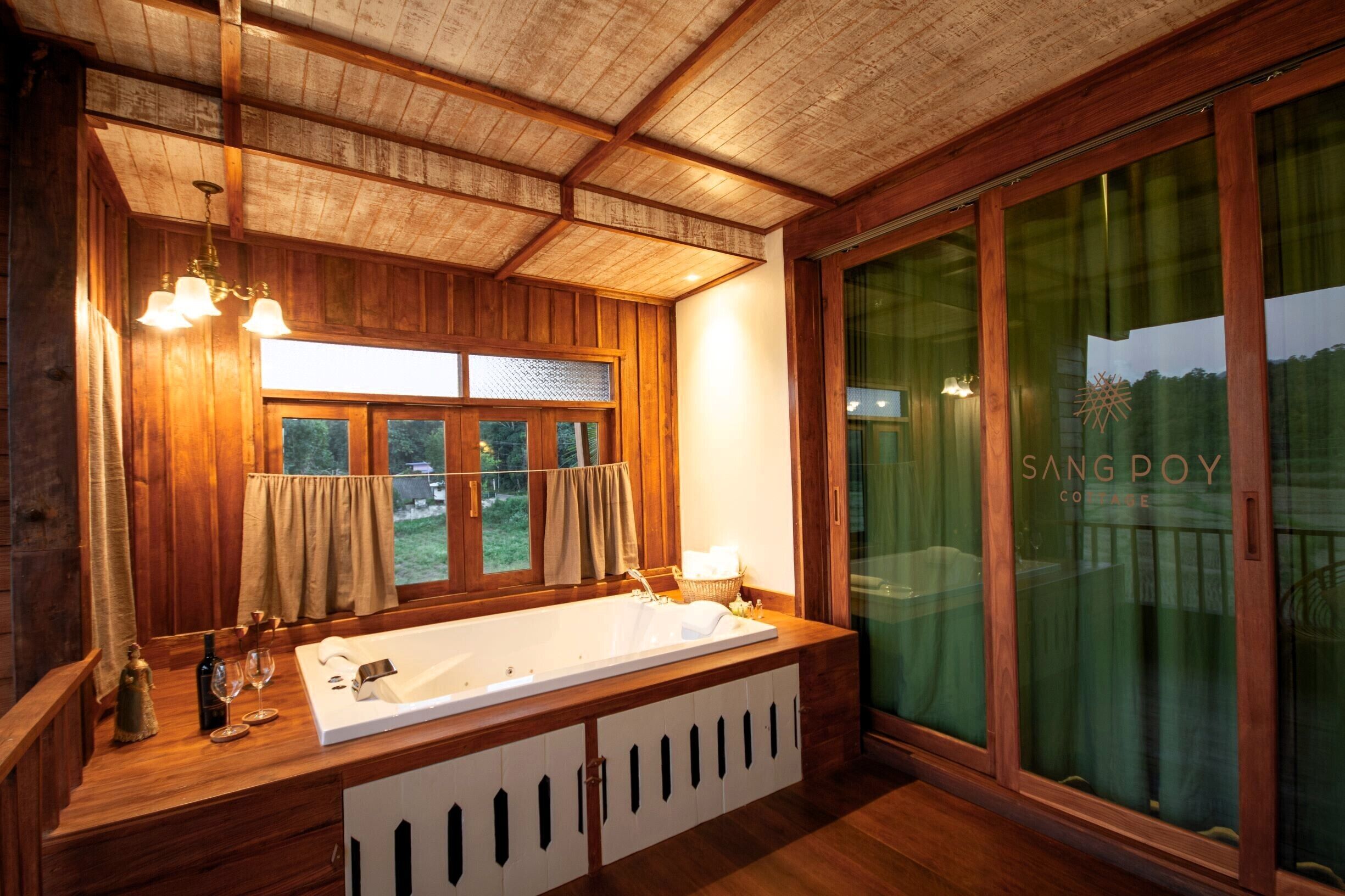 A wooden cabin interior with a large bathtub, wooden cabinets, and a large window with curtains.