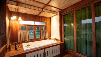 A wooden cabin interior with a large bathtub, wooden cabinets, and a large window with curtains.