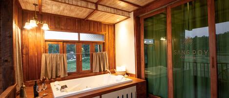 Interior de una cabaña de madera con una bañera grande, armarios de madera y un ventanal con cortinas.