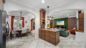 A modern living space with a kitchen, dining area, and a cozy seating area with a TV and green wall. - Lakehouse Escape|Pool|HotTub|Game Suite|Sleeps 20 (Tampa)