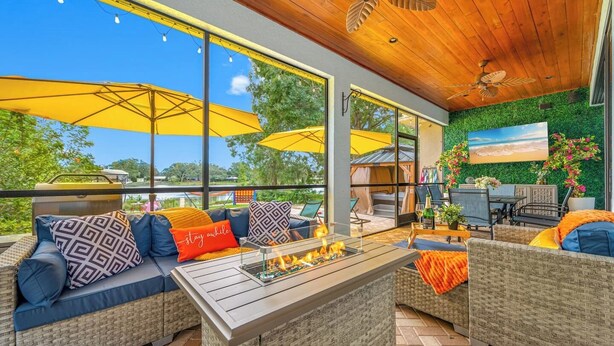 An outdoor patio with wicker furniture, a fire feature, and large windows offering a view of the outdoors. - Lakehouse Escape|Pool|HotTub|Game Suite|Sleeps 20 (Tampa)