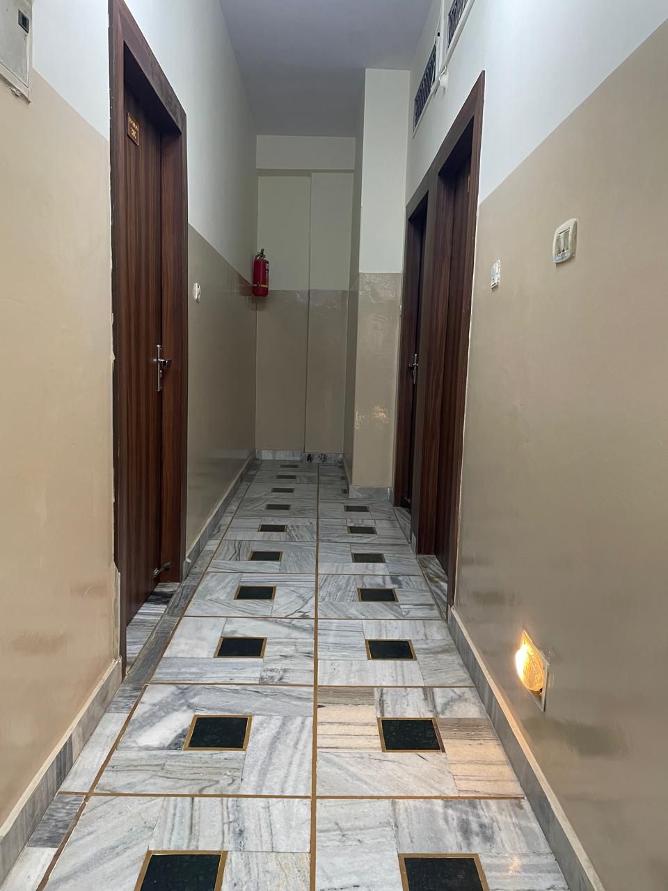 Un corridoio con pavimento in marmo, porte in legno e un estintore a parete.