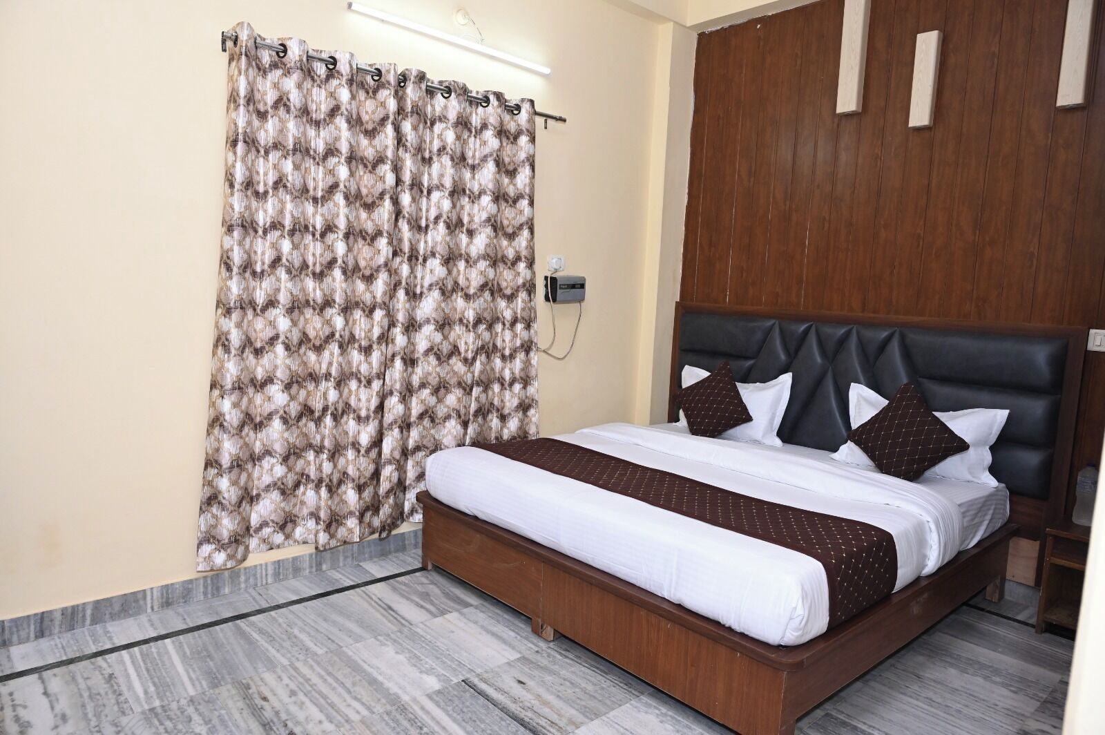 A hotel room with a bed, wooden headboard, and a patterned curtain.