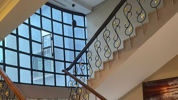 A staircase with a wooden handrail and black metal balusters with golden accents. - Hotel Heritage (Varanasi)