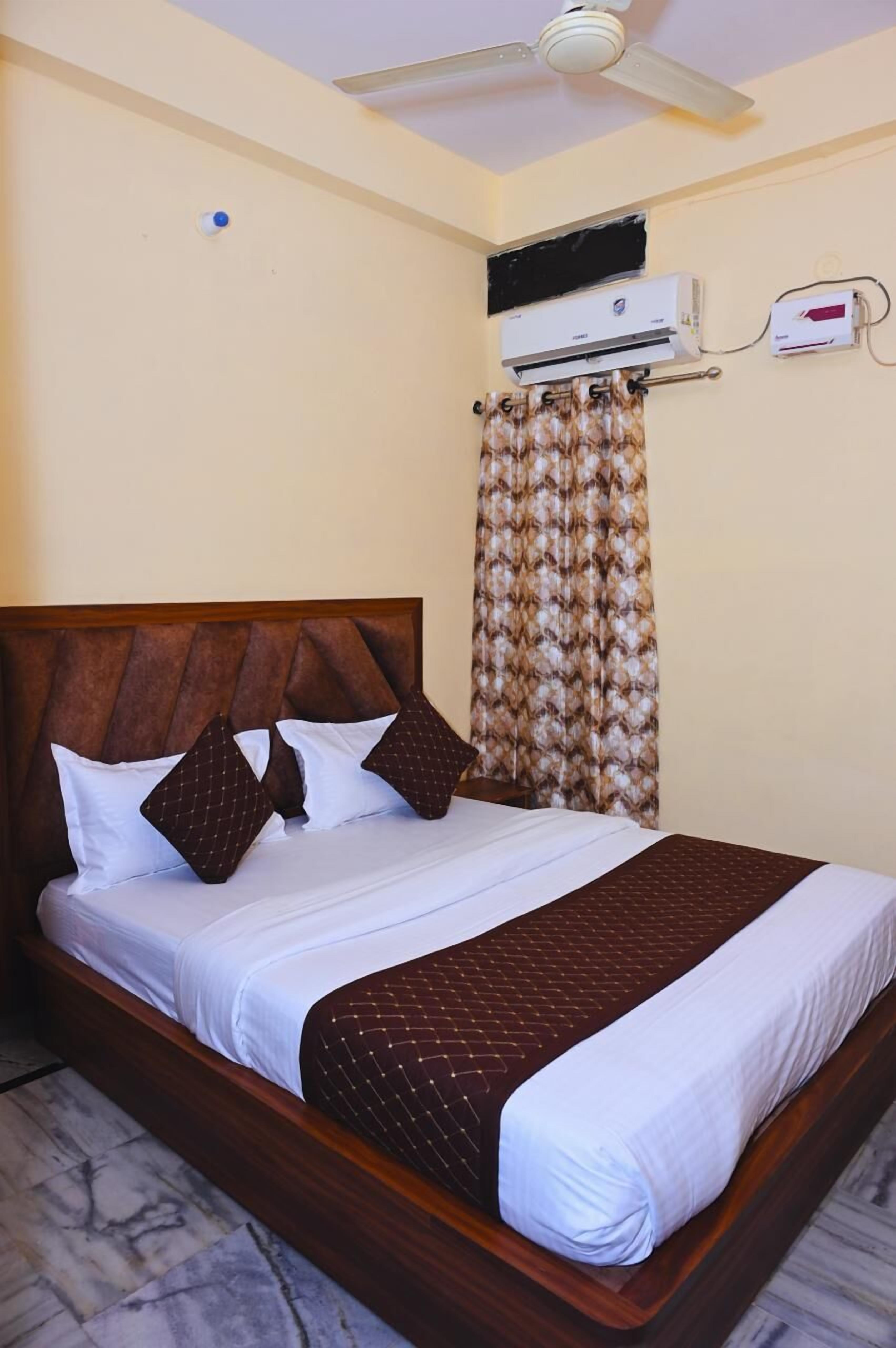 Een hotelkamer met een bed, een plafondventilator, een airconditioningsysteem en een kamerbedekking met patroon.