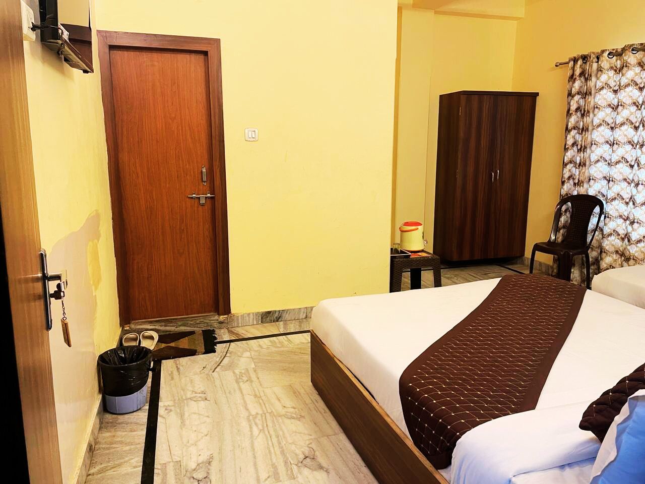 Habitación de hotel con una cama, una puerta de madera, un armario, una silla y una mesita con una lámpara.