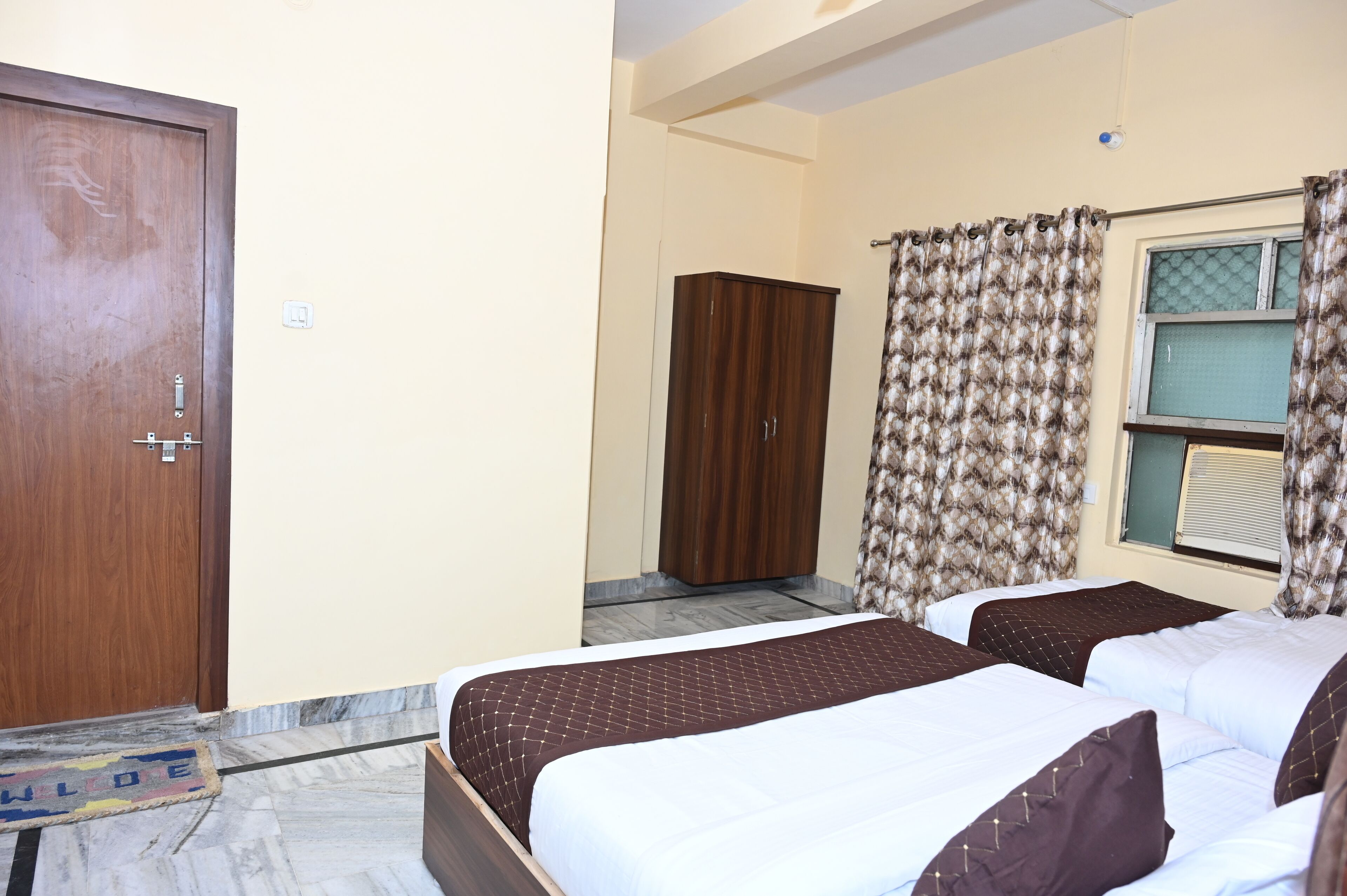 A hotel room with two beds, a wardrobe, a window with curtains, and a door.