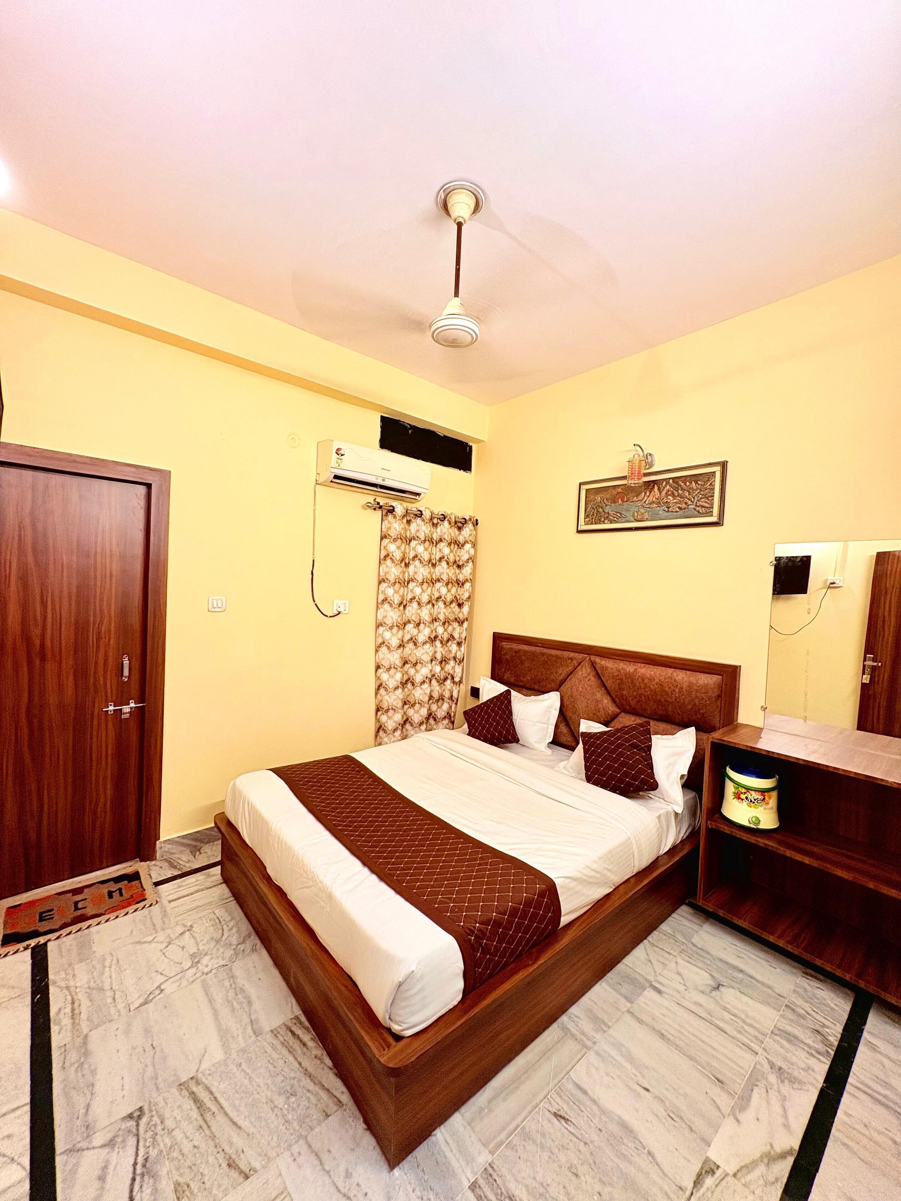 A hotel room with a bed, wooden wardrobe, air conditioning unit, and a ceiling fan.
