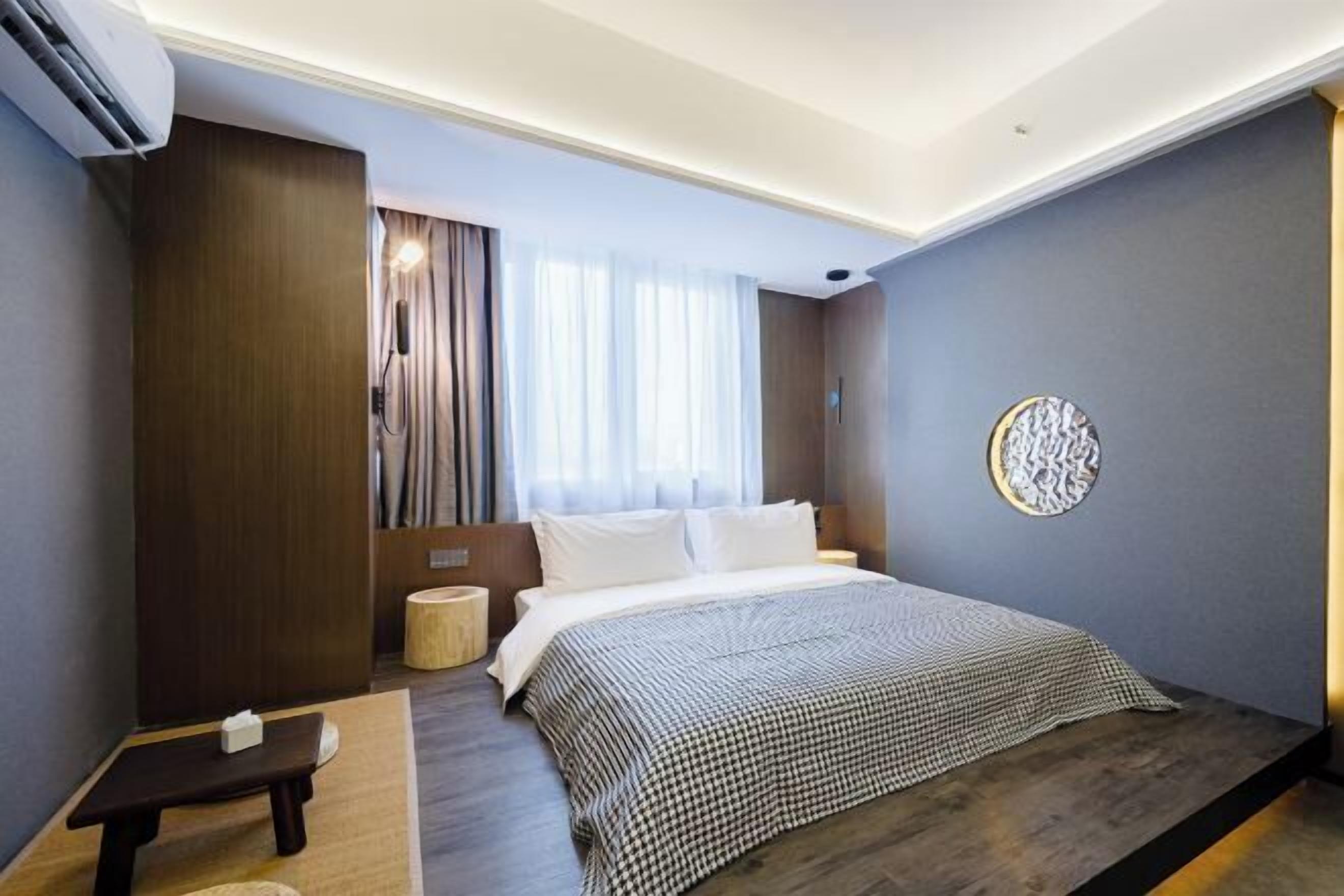 Habitación de hotel moderna con una cama grande, una mesita de noche, un taburete pequeño y un adorno en la pared.