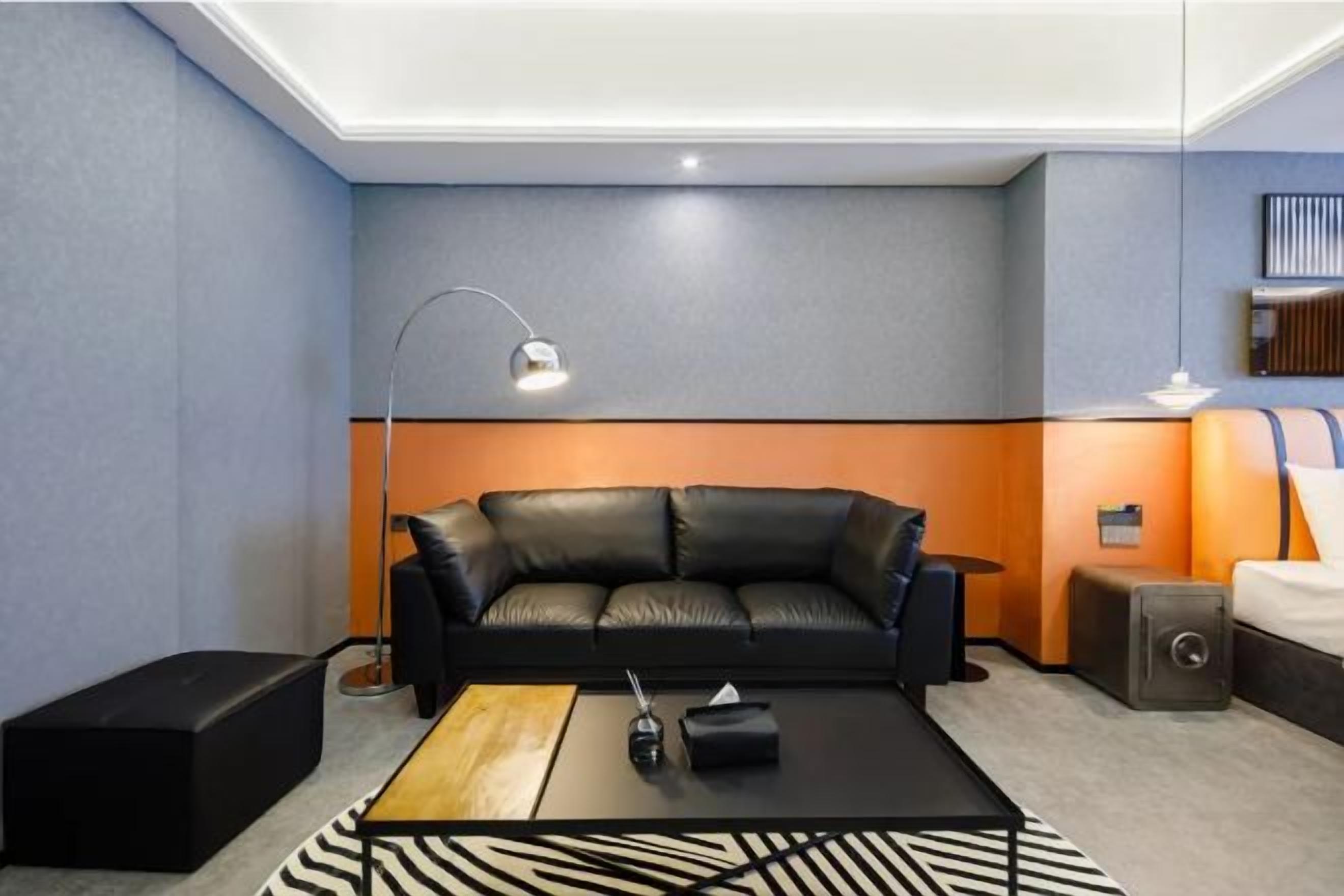 A modern hotel room with a black leather sofa, a wooden coffee table, a lamp, and a small side table.