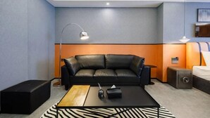 Ein modernes Hotelzimmer mit einem schwarzen Ledersofa, einem Holztisch, einer Lampe und einem kleinen Beistelltisch.