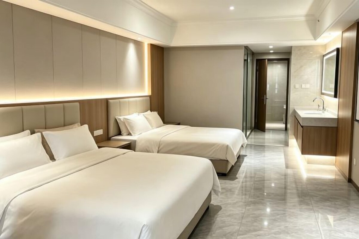 A hotel room with two beds, a bathroom, and a corridor leading to another room.