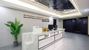 A hotel reception area with a reception desk, a potted plant, and a wall-mounted sign.