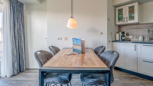 A dining area with a wooden table, six chairs, a pendant light, and a view of the kitchen with cabinets and a countertop. - Nice Apartment Near the Center of De Koog (De Koog)