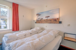 Ein Doppelzimmer mit zwei Betten, einem fenster mit Vorhängen, einem Gemälde einer Savannenlandschaft und einem Nachttisch.