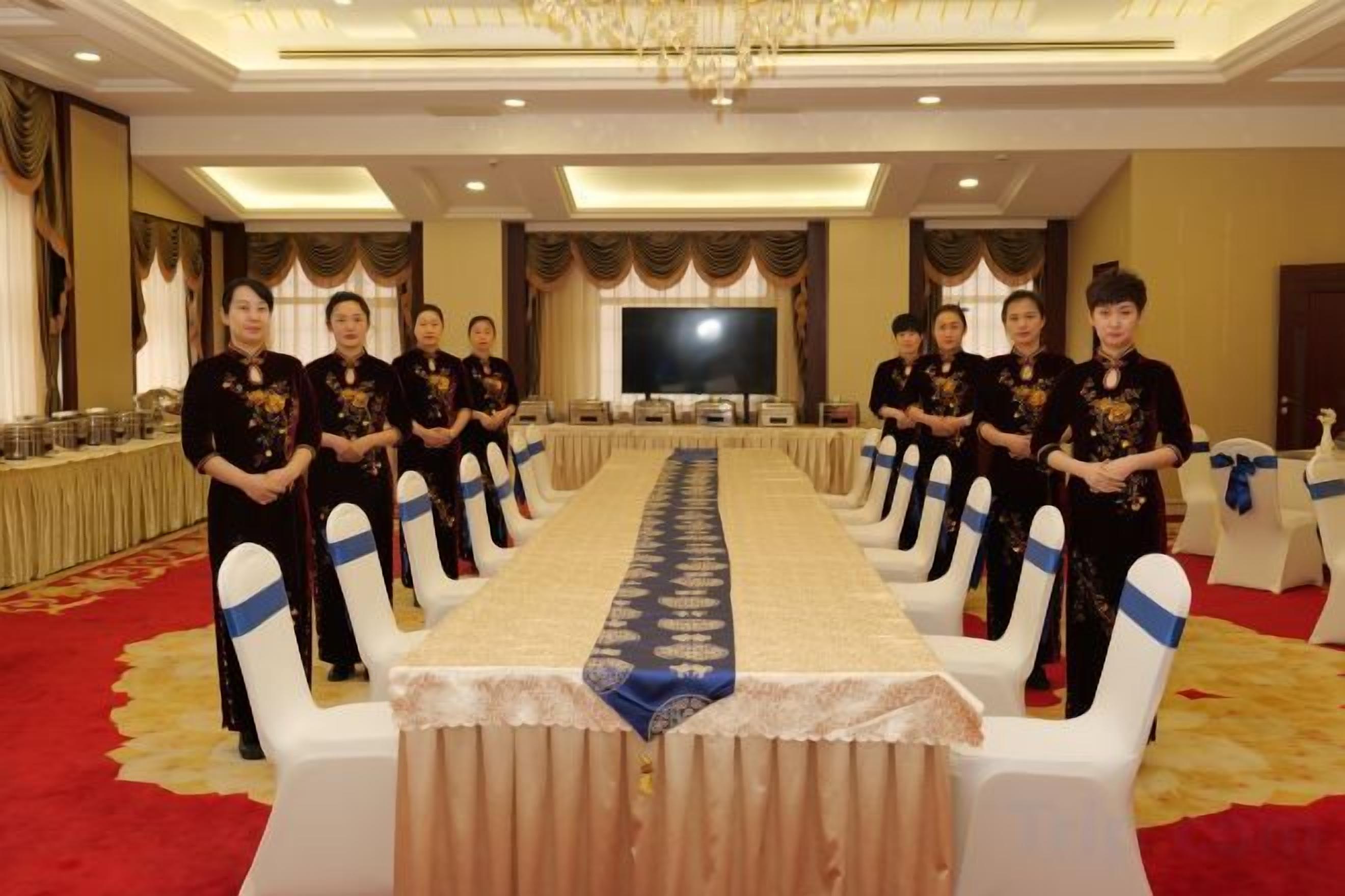 Uma sala de conferências com uma mesa comprida, cadeiras brancas e um tapete vermelho.