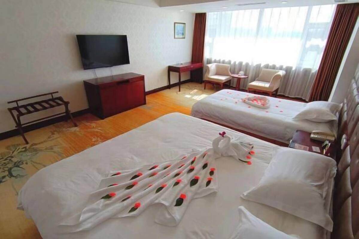 Une chambre d’hôtel avec deux lits, une télévision, un bureau, une chaise et une fenêtre avec des rideaux.