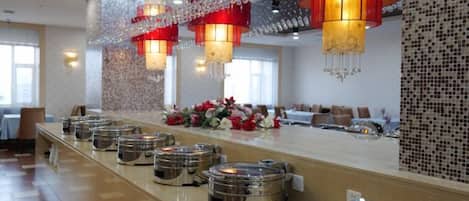 A long buffet line with round serving stations, a floral centerpiece, and decorative red lanterns.