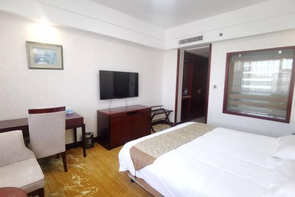 Une chambre d’hôtel avec un lit, un bureau, une chaise, une télévision et une fenêtre.