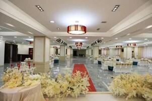 Un salón de banquetes con mesas redondas, alfombra roja y arreglos florales.