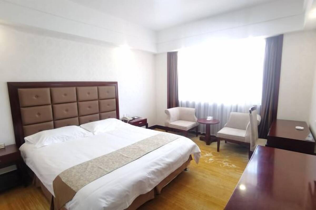 Une chambre d’hôtel avec un grand lit, un bureau, une chaise et une fenêtre avec des rideaux.