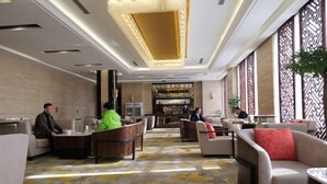 Un hall d’hôtel comprenant des espaces aménagés avec des sièges, un comptoir d’accueil et des panneaux muraux décoratifs.