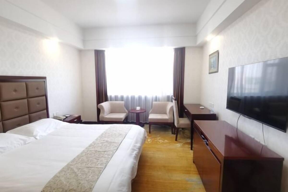 Une chambre d’hôtel comprenant un lit, deux fauteuils, un bureau, une télévision et une fenêtre avec des rideaux.