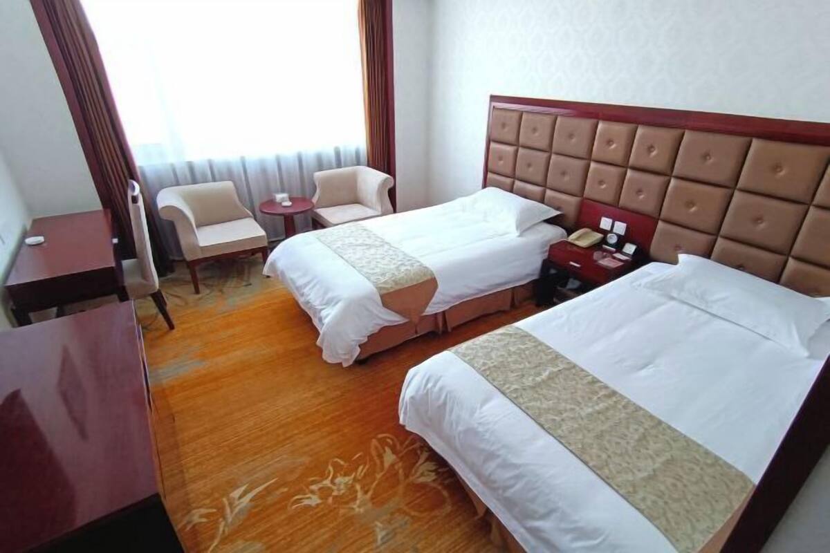Une chambre d’hôtel avec deux lits, un coin salon comprenant une chaise et une petite table, ainsi qu’un bureau.