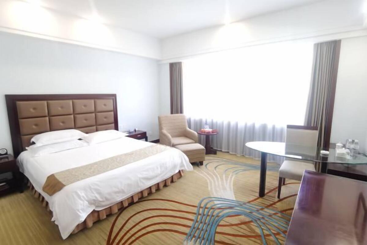 Une chambre d’hôtel avec un grand lit, une chaise, une petite table et une vue sur l’extérieur par la fenêtre.